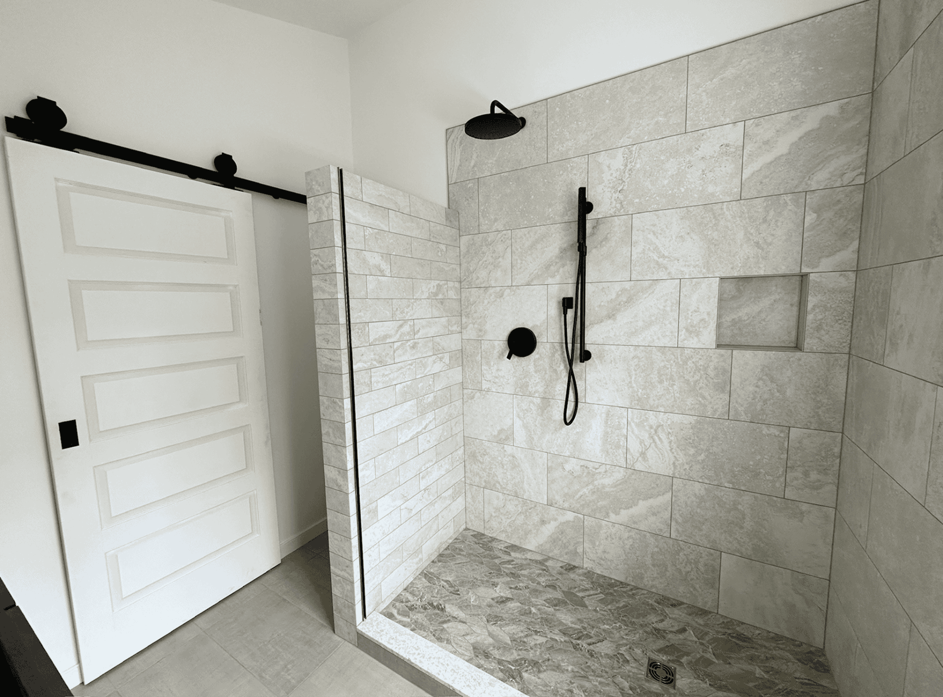 Contemporary walk-in shower with beige tiles and black fixtures in a modern bathroom.
